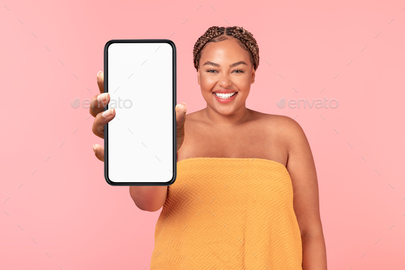 Modern beauty app. Happy black body positive lady showing cellphone with blank screen, pink