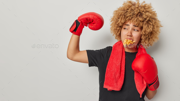 Horizontal shot of young athlete woman exercises in gym raises arm and shows biceps prepares for box