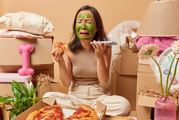 Upset crying woman holds piece of pizza and smartphone has bad mood undergoes beauty procedures pose