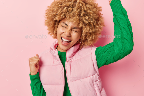 Overjoyed Curly Haired Woman Makes Winner Gesture Celebrates Victory Keeps Arms Raised Up 