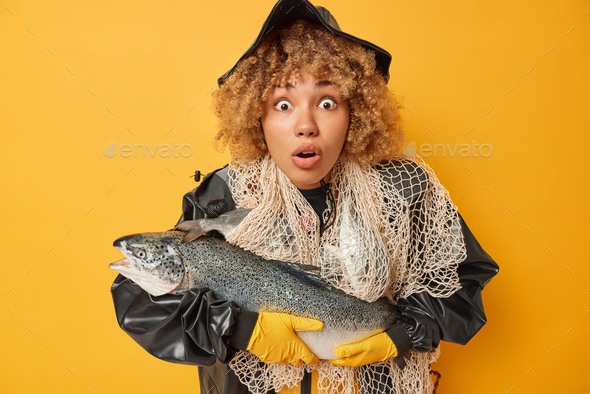 Speechless woman with curly hair holds big caught salmon stares impressed holds breath from amazemen