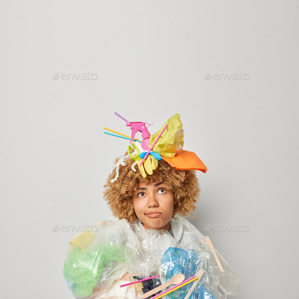 Confused curly haired female volunteer covered with plastic garbage doesnt know how to save planet f