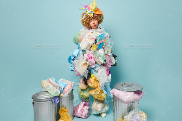 Upset tired woman poses around garbage makes clothes from plastic wastes cleans out planet from poll