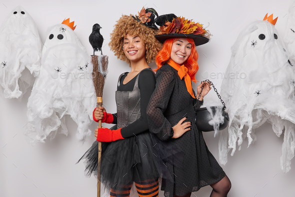 Holiday celebration concept. Two positive witches stand back to each other wear black hats and dress