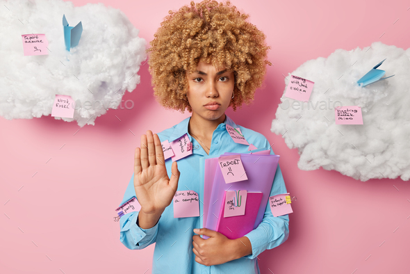 Displeased female student makes stop gesture asks not to bother her dressed in blue shirt holds fold