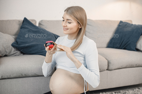 Pregnant lady sitting near a sofa in living room and brushing her hair