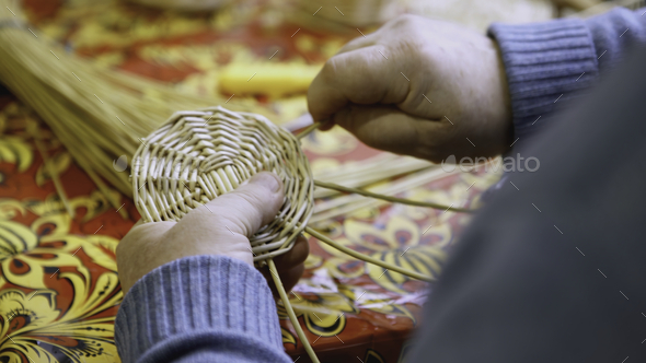Hands weaving the bottom of a straw basket. ART. A man weaves a round part  of straw and twigs with Stock Photo by BlackWhaleMedia
