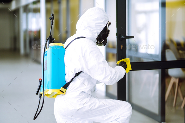 Cleaning and disinfection of office to prevent COVID-19, Man in protective hazmat suit washes office