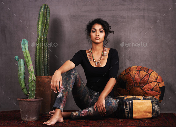 Ethnically at ease. Studio portrait of a beautiful young woman sitting amongst cacti and cushions.