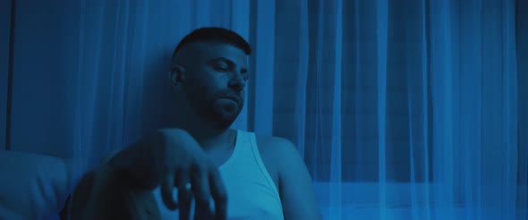 An adult man apathetically sitting in the bedroom, staring to nowhere. alt