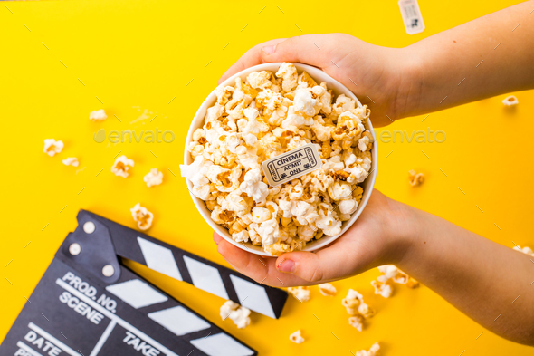 Popcorn viewed from above on yellow background. Child eating pop-corns. Human hand. Cinema