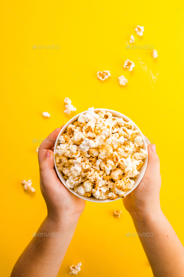 Popcorn viewed from above on yellow background. Child eating pop-corns. Human hand.