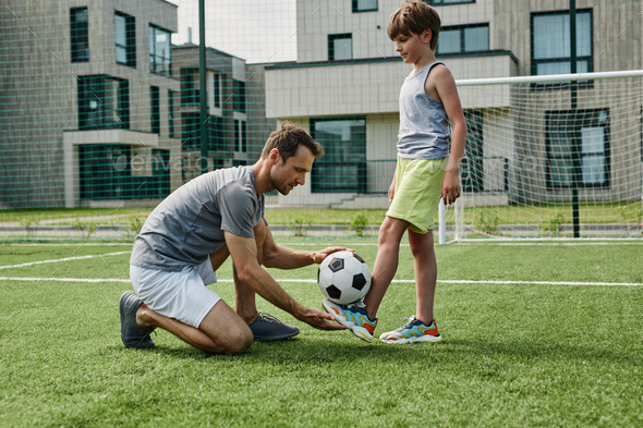 Side view young father teaching son football in outdoor court