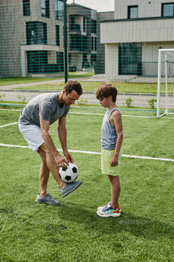 Side view loving father teaching son football in outdoor court