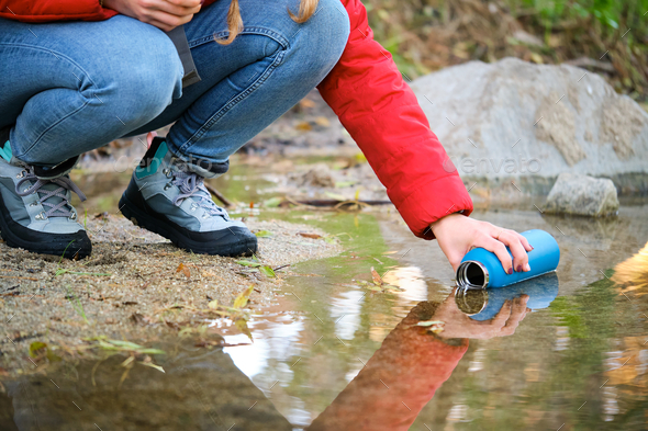 Unrecognizable trekker filling water bottle of raw water in a river.