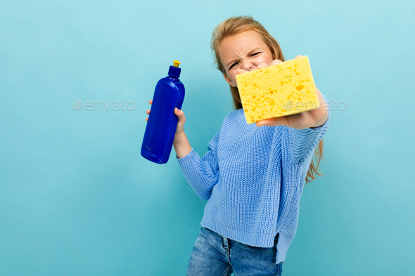 Girl is going to wash the dishes with washcloth and detergent isolated on blue background
