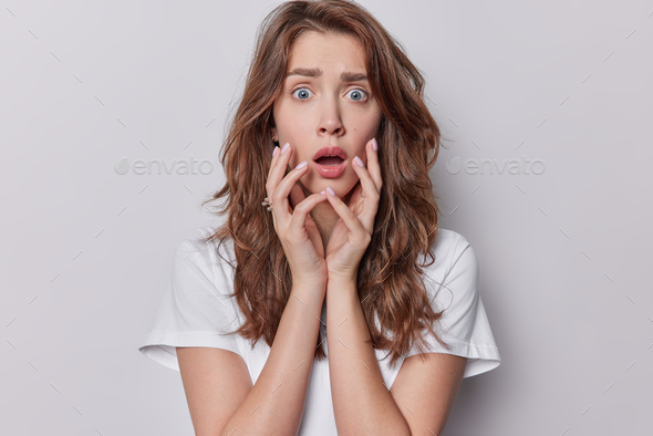 Scared shocked European woman holds breath from amazement being afraid of something wears casual