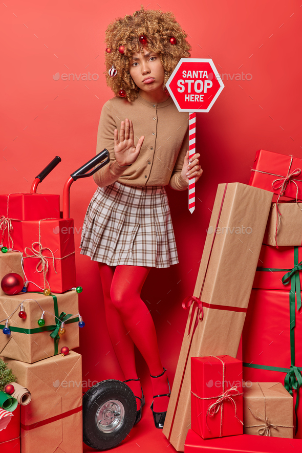 Serious displeased woman keeps palm raised in denial gesture asks to stop there holds traffic sign