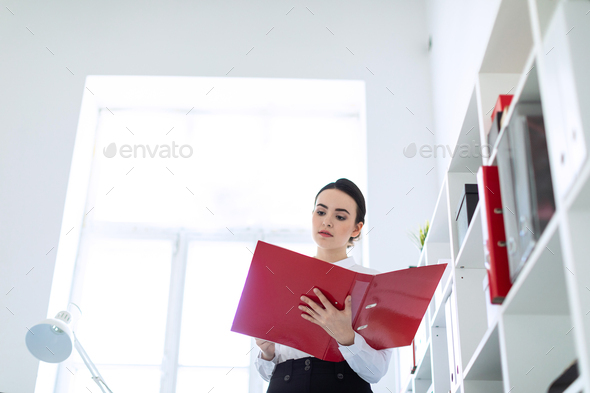 Young girl in the office near the rack and scrolls through the folder with the documents.