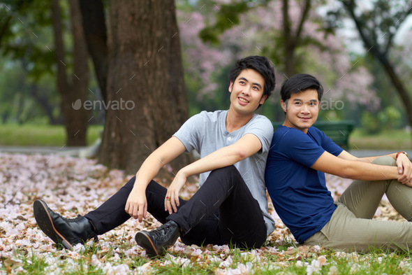 Cute asian couple sitting in the park smiling and looking at