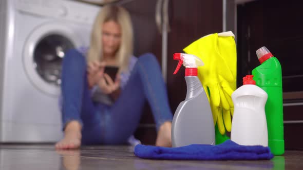woman sitting on floor with her phone out of focus. Bottles of cleaning agent alt