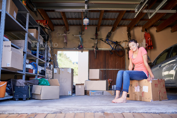 Sitting amongst the storage. Portrait of a young girl sitting on a box in a garage.