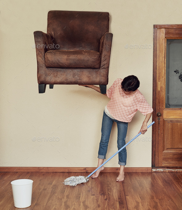 No task is too difficult for her. Shot of a woman lifting a couch to mop underneath it.