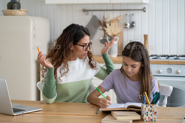 Optimistic focused teenage girl with woman nanny studying school curriculum sits at kitchen table - Stock Photo - Images
