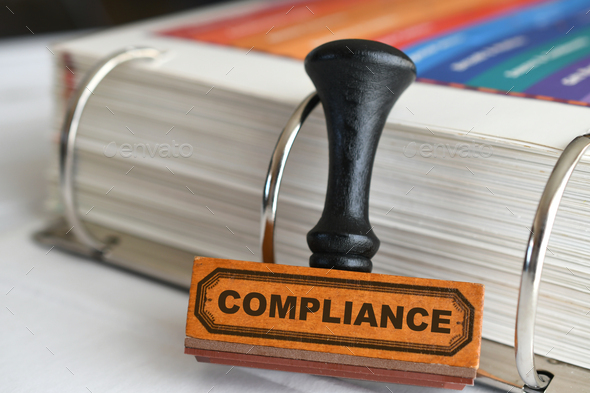 Compliance rubber stamp by binder of rules guidelines, changing procedures to adhere to regulations - Stock Photo - Images