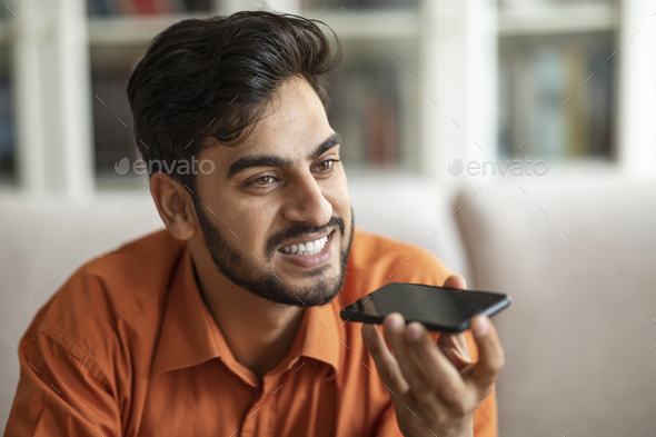 Closeup of happy arab man recording voice mail on smartphone