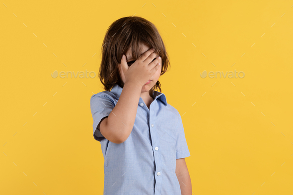 Disappointed cute little boy showing facepalm gesture, can't believe what he sees, orange studio - Stock Photo - Images