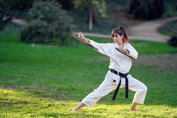 Karate fighter woman in kimono and black belt standing in karate pose while training outdoors.