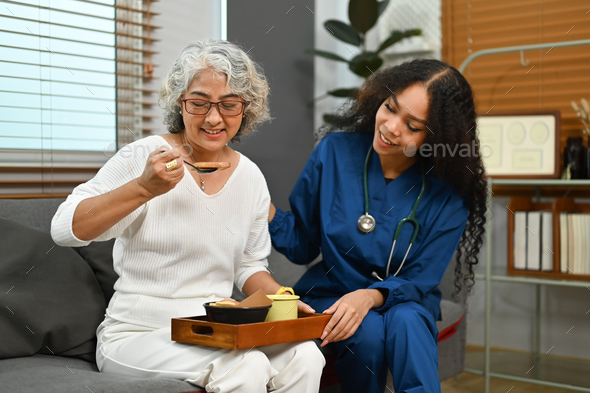 Photo of elderly woman having healthy nutrition breakfast meal with professional helpful caregiver.