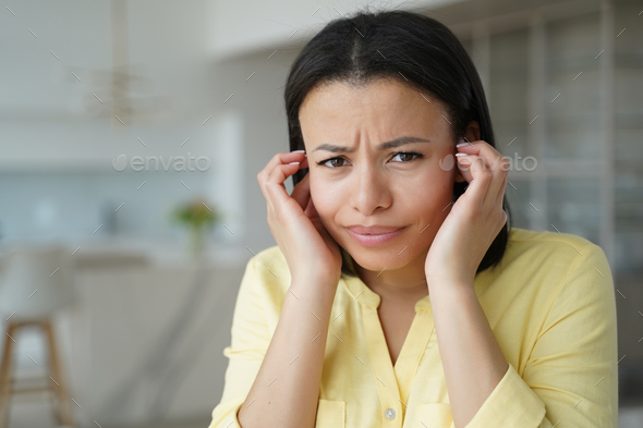 Irritated female stuck her fingers in ears, suffering from loud noise at home or feels ear pain