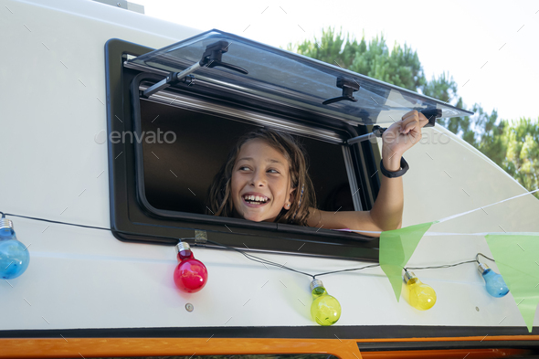 The happy girl sticks her head out of the van window on a wonderful day at camp. Van life concept.