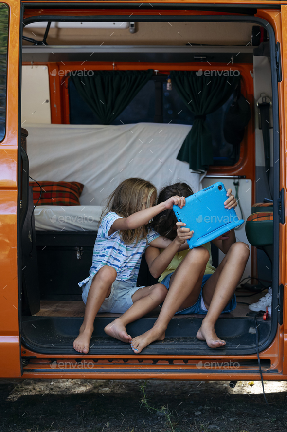 Two brothers fighting over the tablet on a wonderful day camping in a van. Van life concept.