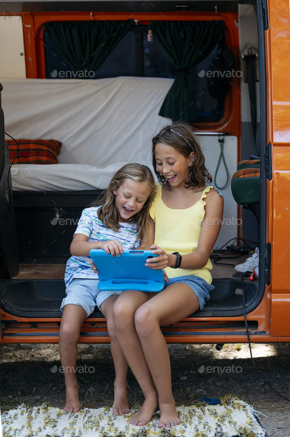 Two sibling boys using the tablet on a wonderful day camping in a van. Van life concept.