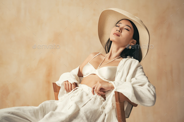 Studio shot of relaxed asian elegant woman with closed eyes leaning on back of chair, sun tanning