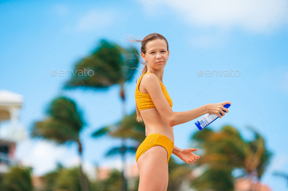 Adorable teen girl yellow bikini applying sunscreen cream the beach Stock Photo by travnikovstudio