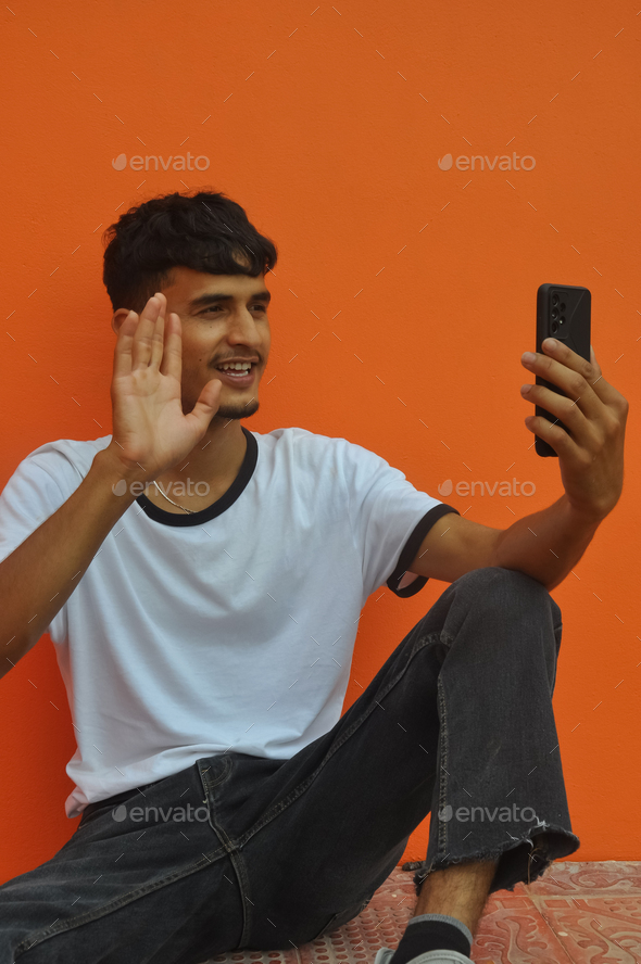 A happy young guy saying hello with waving his hand to someone while video call