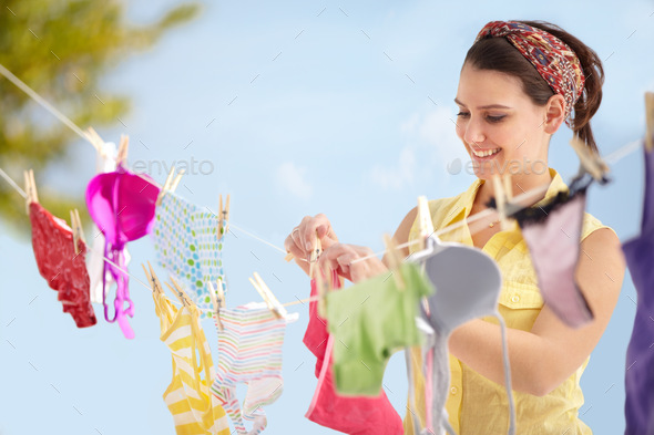 Its laundry day. Attractive young woman hanging up her washing on a line outside.