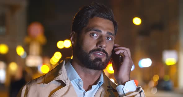 Bokeh Shot of Young Indian Man Talking on Smartphone Outdoors at Night alt