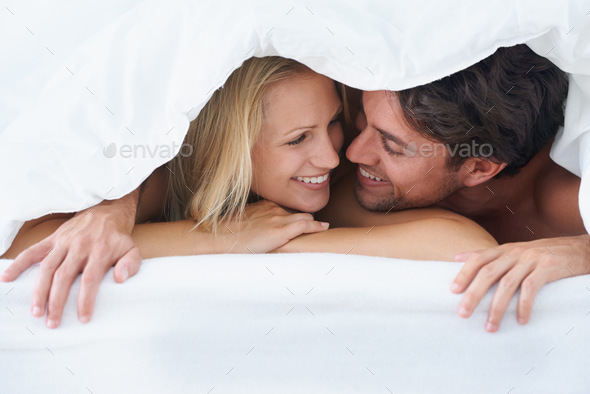 A couple lying under a duvet cover and cuddling affectionately while looking into each others eyes