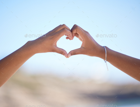 Hands together, heart sign and outdoor at beach, nature and blue sky in blurred background for love