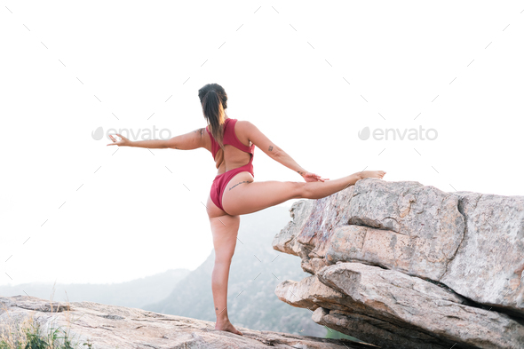 caucasian mature woman doing sport with left leg on the ground and right leg on the big rock