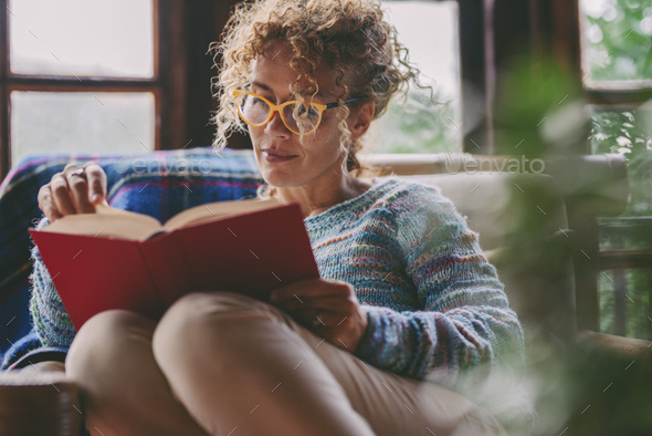 Woman at home sitting and reading a book in relax indoor leisure activity at home. Serene female