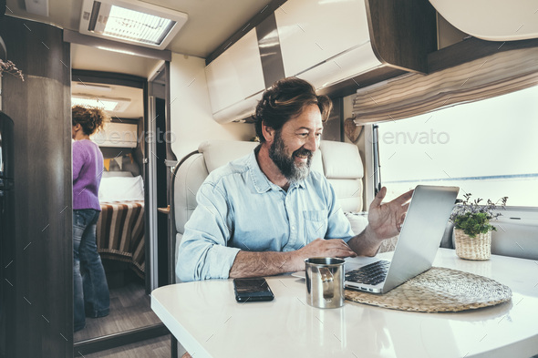 Man and woman living off grid inside a modern camper working on laptop connected online