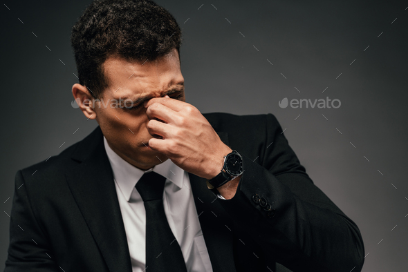 tired african american businessman in wristwatch rubbing his eyes on dark background