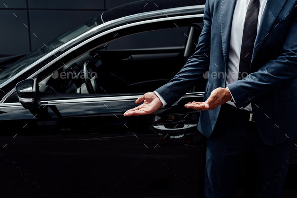 cropped view of african american man in suit pointing at black car door