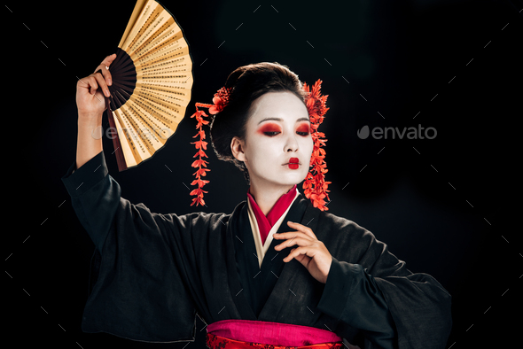 geisha in black kimono with red flowers in hair dancing with traditional asian hand fan isolated on